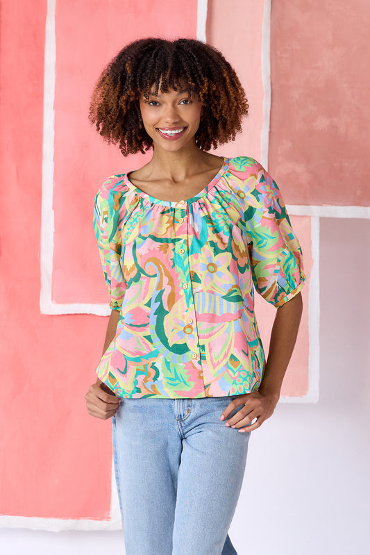 Model wearing a hip-length short sleeve top in a vibrant multicolor floral print, featuring a scoop neckline, button front, swingy silhouette, and short balloon sleeves — CROSBY by Mollie Burch