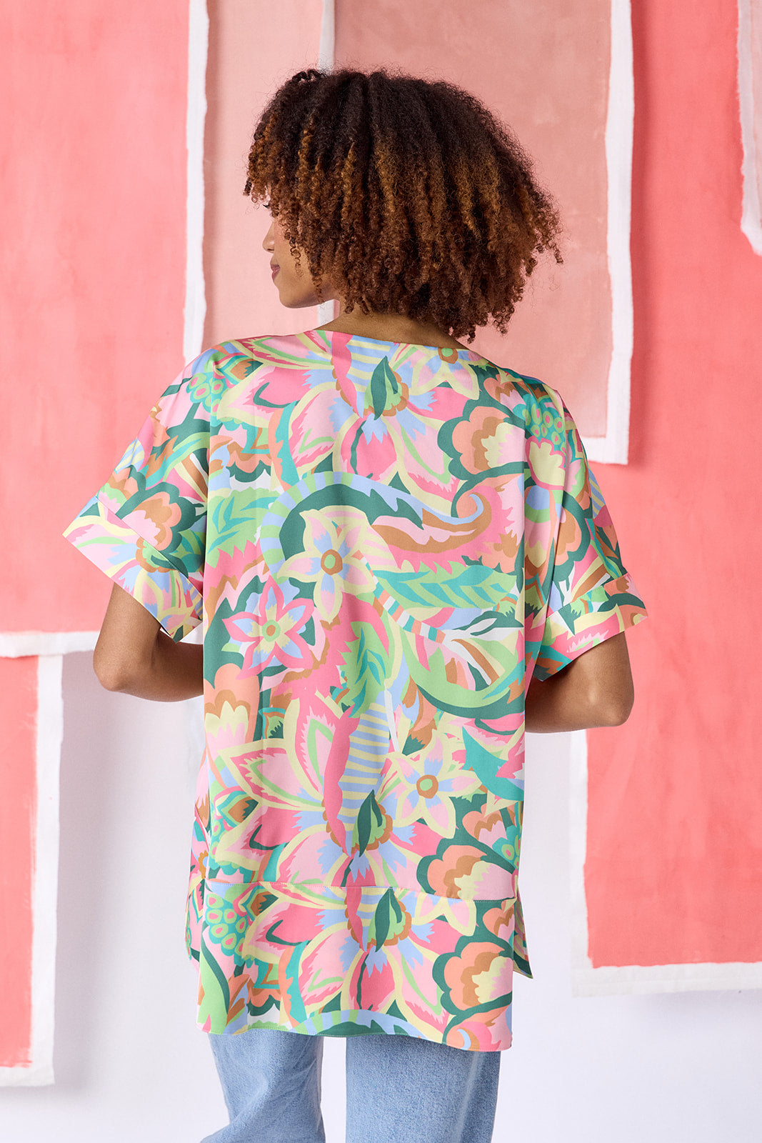 Model wearing top-of-the-thigh length tunic blouse in a vibrant multicolor floral print, featuring a breezy silhouette, split V-neck, and short dolman sleeves with seamed cuffs — CROSBY by Mollie Burch