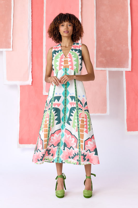 Model wearing ankle-length, sleeveless fit-and-flare dress with a V-neckline and paneled skirt. Features a colorful geometric print in green, coral, light blue, and tan tones — CROSBY by Mollie Burch