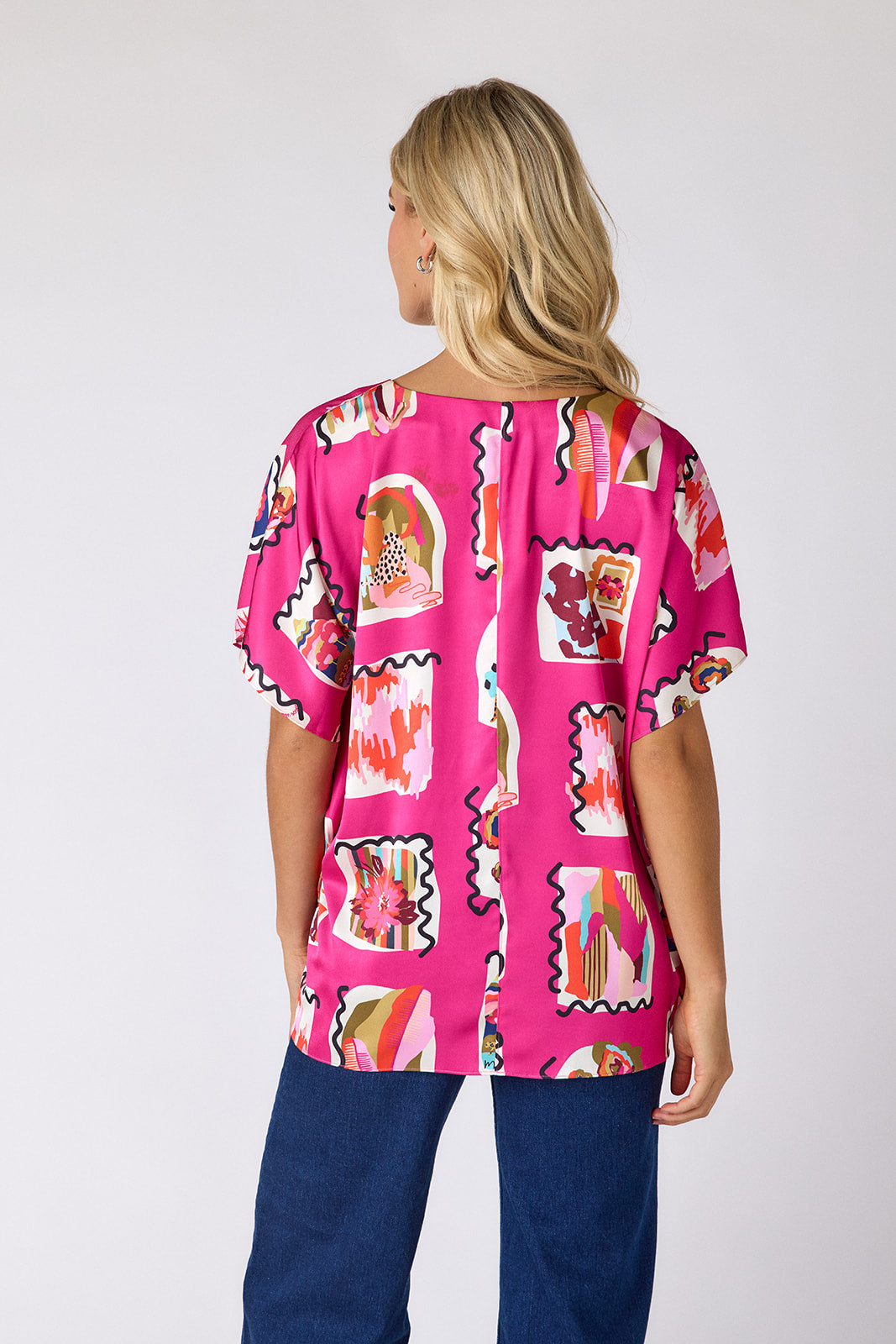 Person wearing a bright pink patterned top with blue pants on a white background