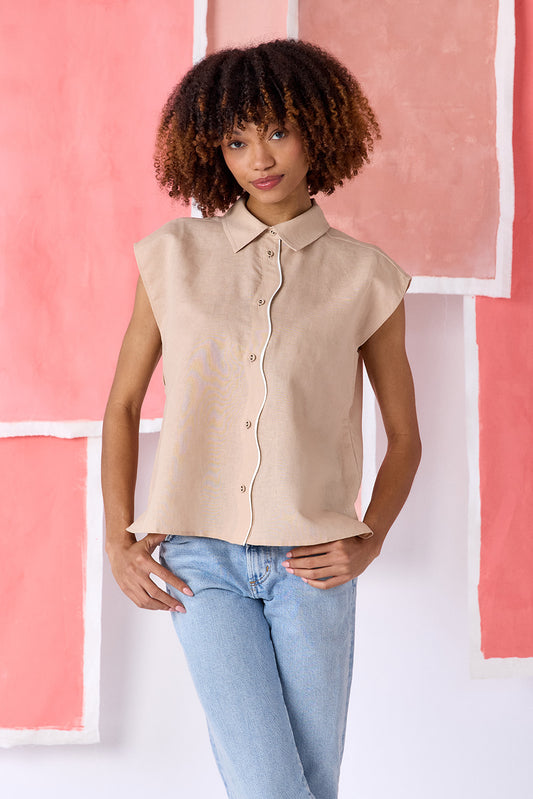 Model wearing beige, hip-length relaxed top with cap sleeves and a squiggle button placket, finished with contrast trim — CROSBY by Mollie Burch