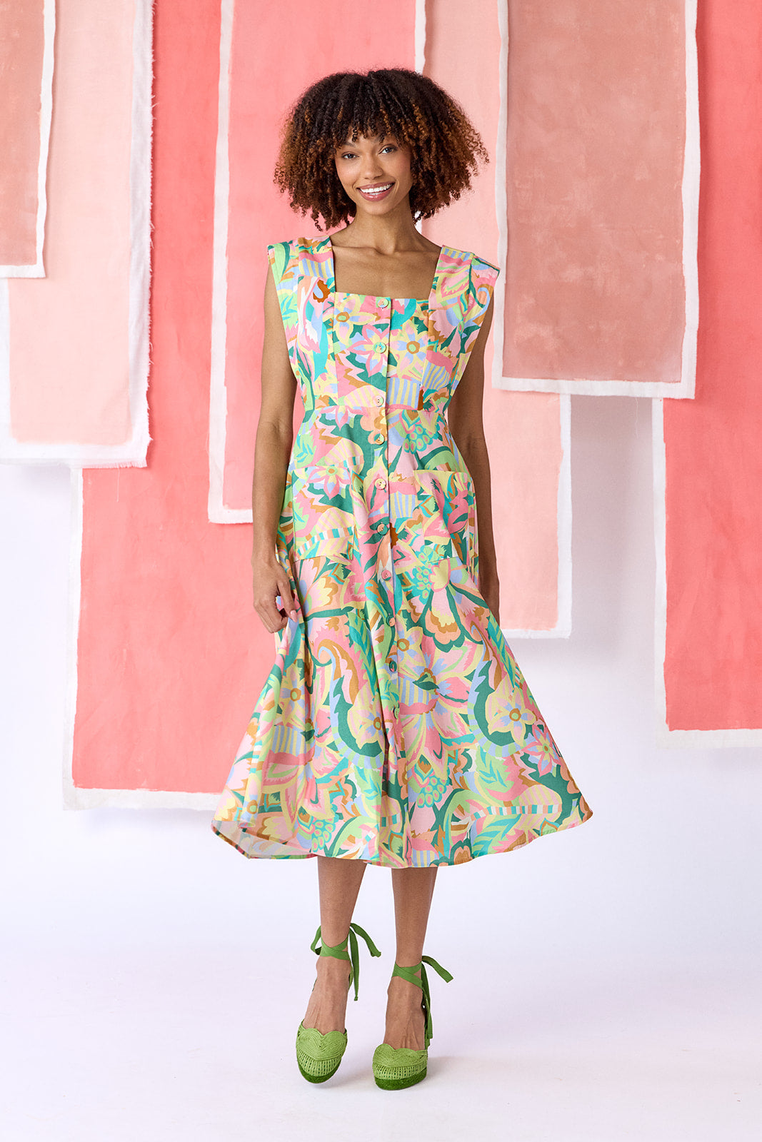 Model wearing a mid-calf length fit-and-flare dress in a vibrant multicolor floral print, featuring a square neckline, cap sleeves, full button front, and a full, swingy skirt — CROSBY by Mollie Burch