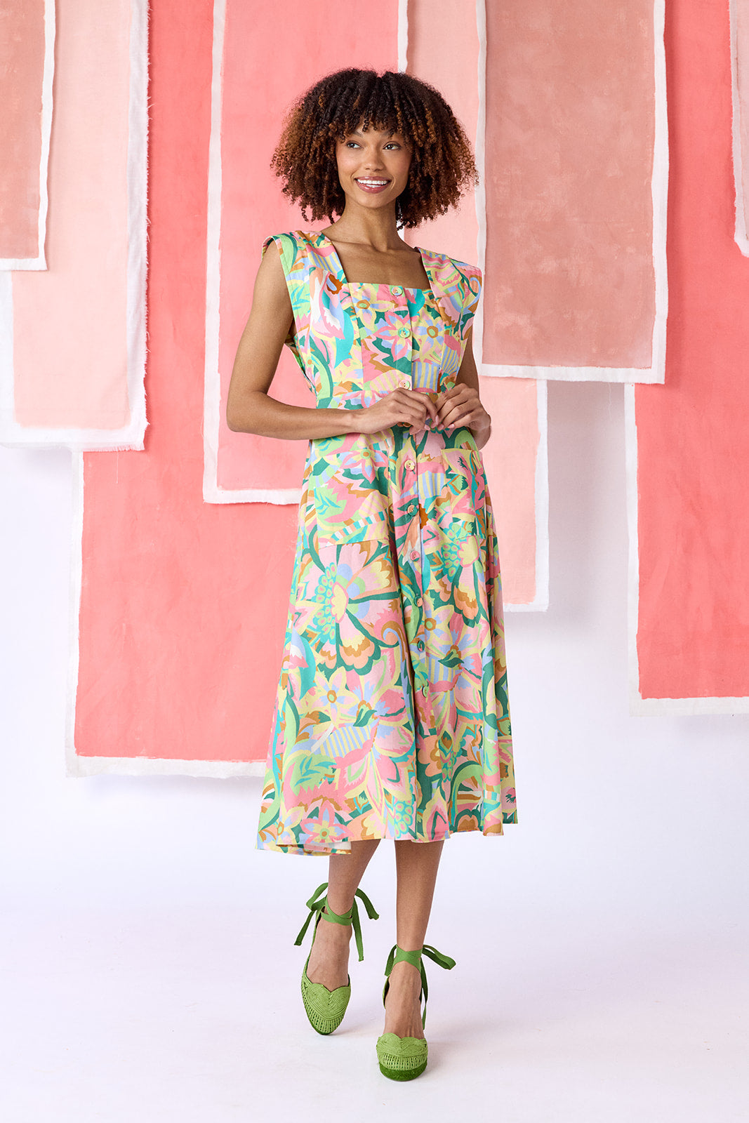 Model wearing a mid-calf length fit-and-flare dress in a vibrant multicolor floral print, featuring a square neckline, cap sleeves, full button front, and a full, swingy skirt — CROSBY by Mollie Burch