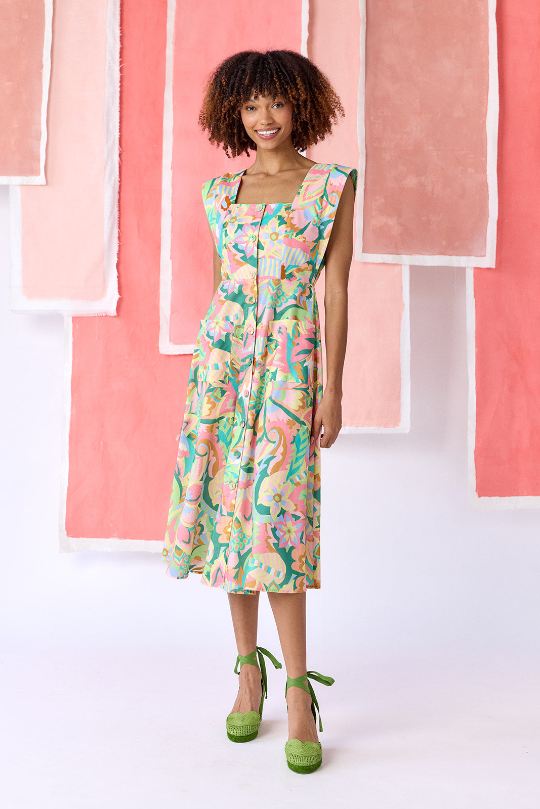 Model wearing a mid-calf length fit-and-flare dress in a vibrant multicolor floral print, featuring a square neckline, cap sleeves, full button front, and a full, swingy skirt — CROSBY by Mollie Burch