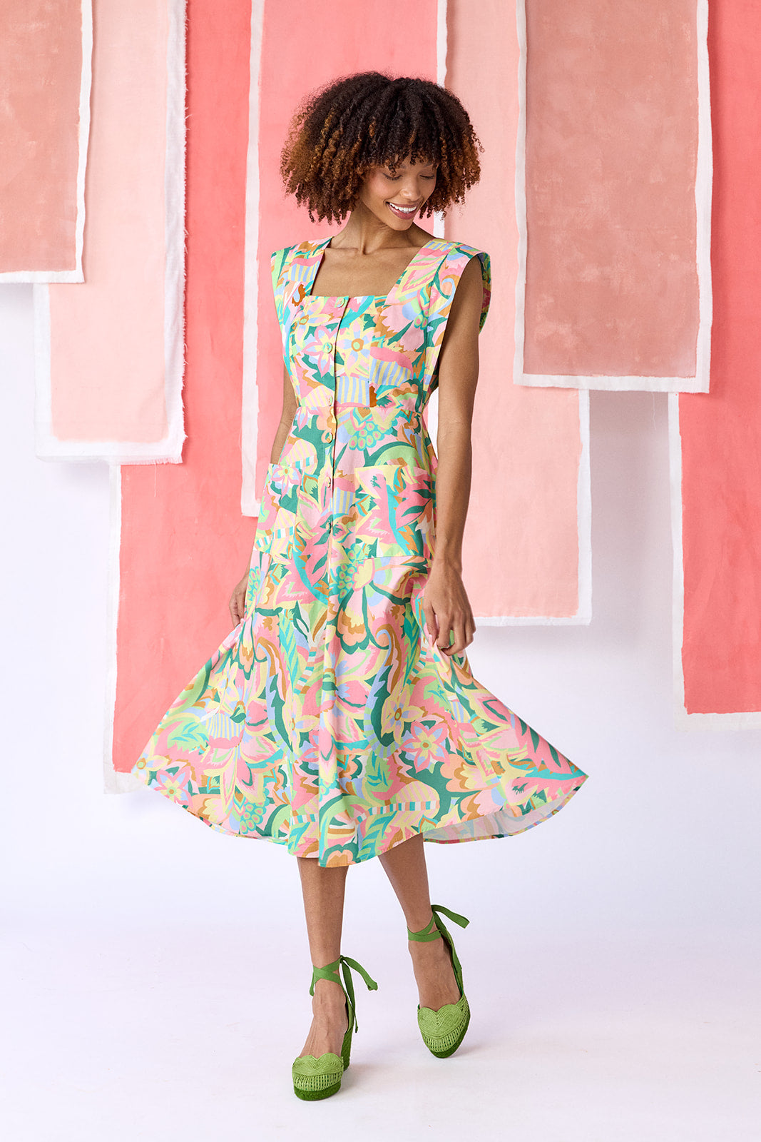 Model wearing a mid-calf length fit-and-flare dress in a vibrant multicolor floral print, featuring a square neckline, cap sleeves, full button front, and a full, swingy skirt — CROSBY by Mollie Burch