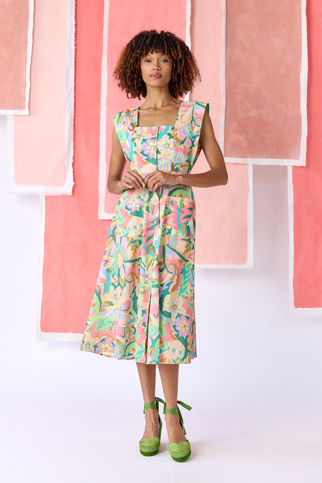 Model wearing a mid-calf length fit-and-flare dress in a vibrant multicolor floral print, featuring a square neckline, cap sleeves, full button front, and a full, swingy skirt — CROSBY by Mollie Burch