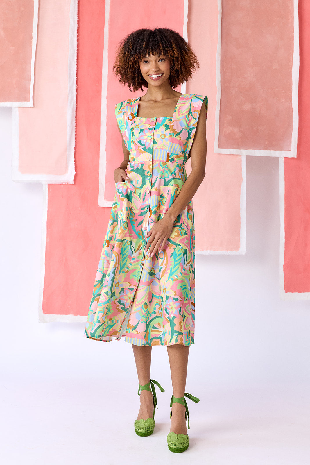 Model wearing a mid-calf length fit-and-flare dress in a vibrant multicolor floral print, featuring a square neckline, cap sleeves, full button front, and a full, swingy skirt — CROSBY by Mollie Burch