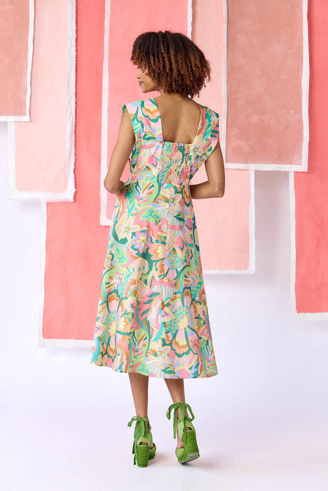 Model wearing a mid-calf length fit-and-flare dress in a vibrant multicolor floral print, featuring a square neckline, cap sleeves, full button front, and a full, swingy skirt — CROSBY by Mollie Burch