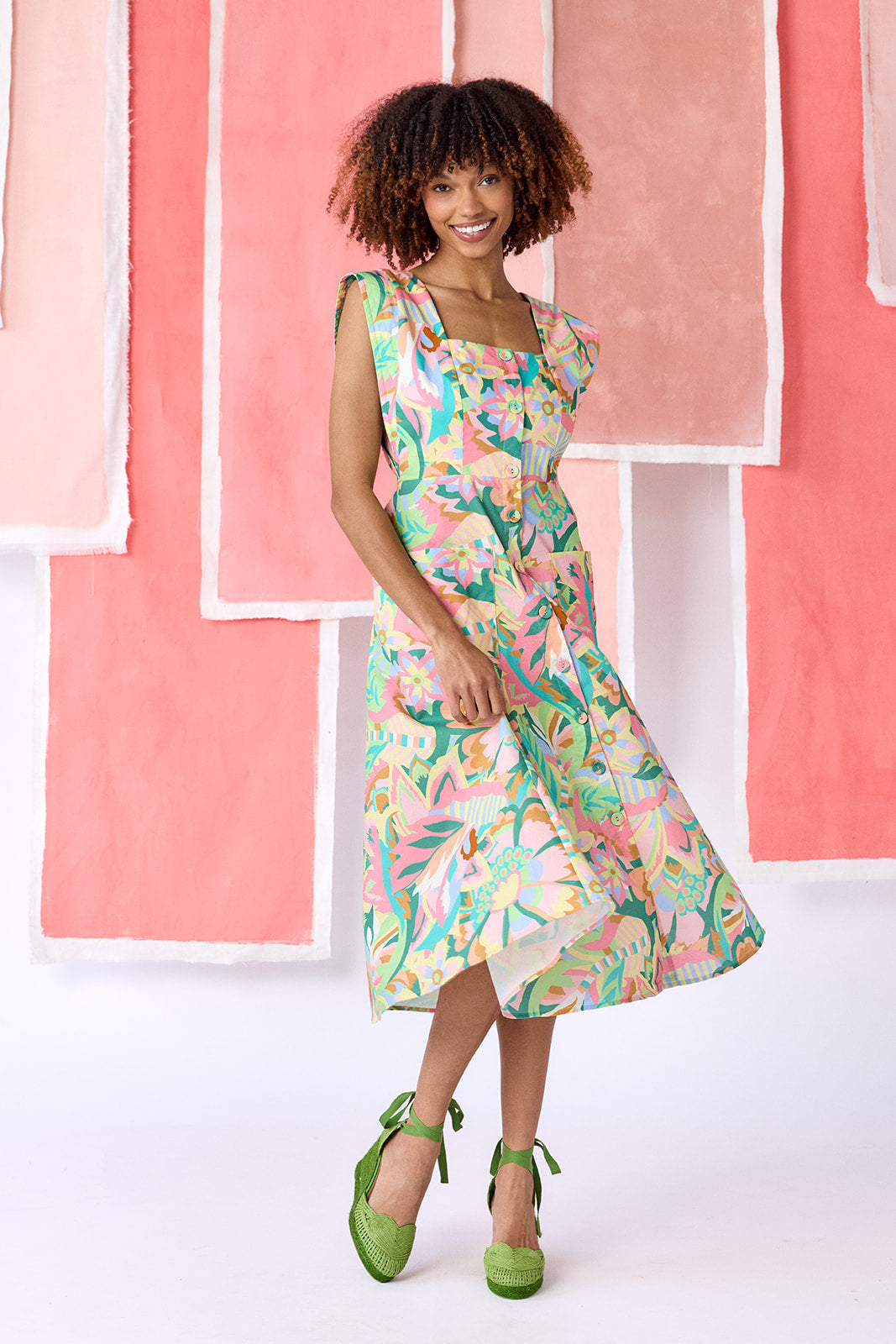 Model wearing a mid-calf length fit-and-flare dress in a vibrant multicolor floral print, featuring a square neckline, cap sleeves, full button front, and a full, swingy skirt — CROSBY by Mollie Burch