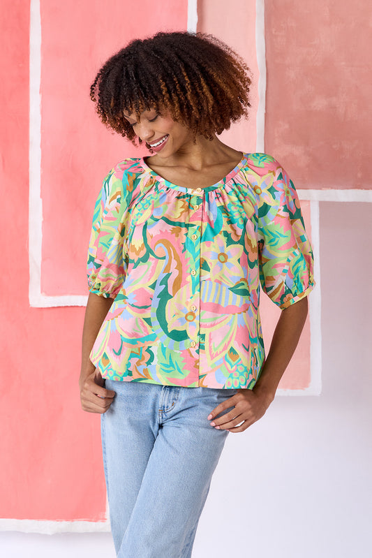 Model wearing a hip-length short sleeve top in a vibrant multicolor floral print, featuring a scoop neckline, button front, swingy silhouette, and short balloon sleeves — CROSBY by Mollie Burch