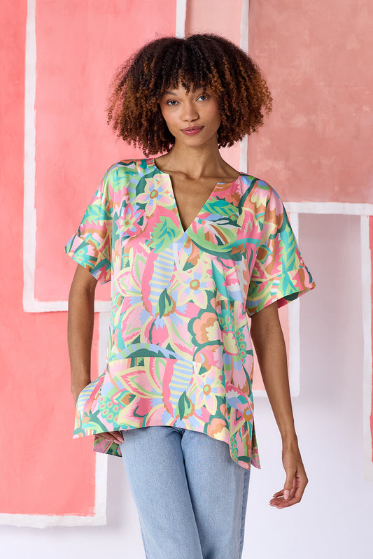 Model wearing top-of-the-thigh length tunic blouse in a vibrant multicolor floral print, featuring a breezy silhouette, split V-neck, and short dolman sleeves with seamed cuffs — CROSBY by Mollie Burch