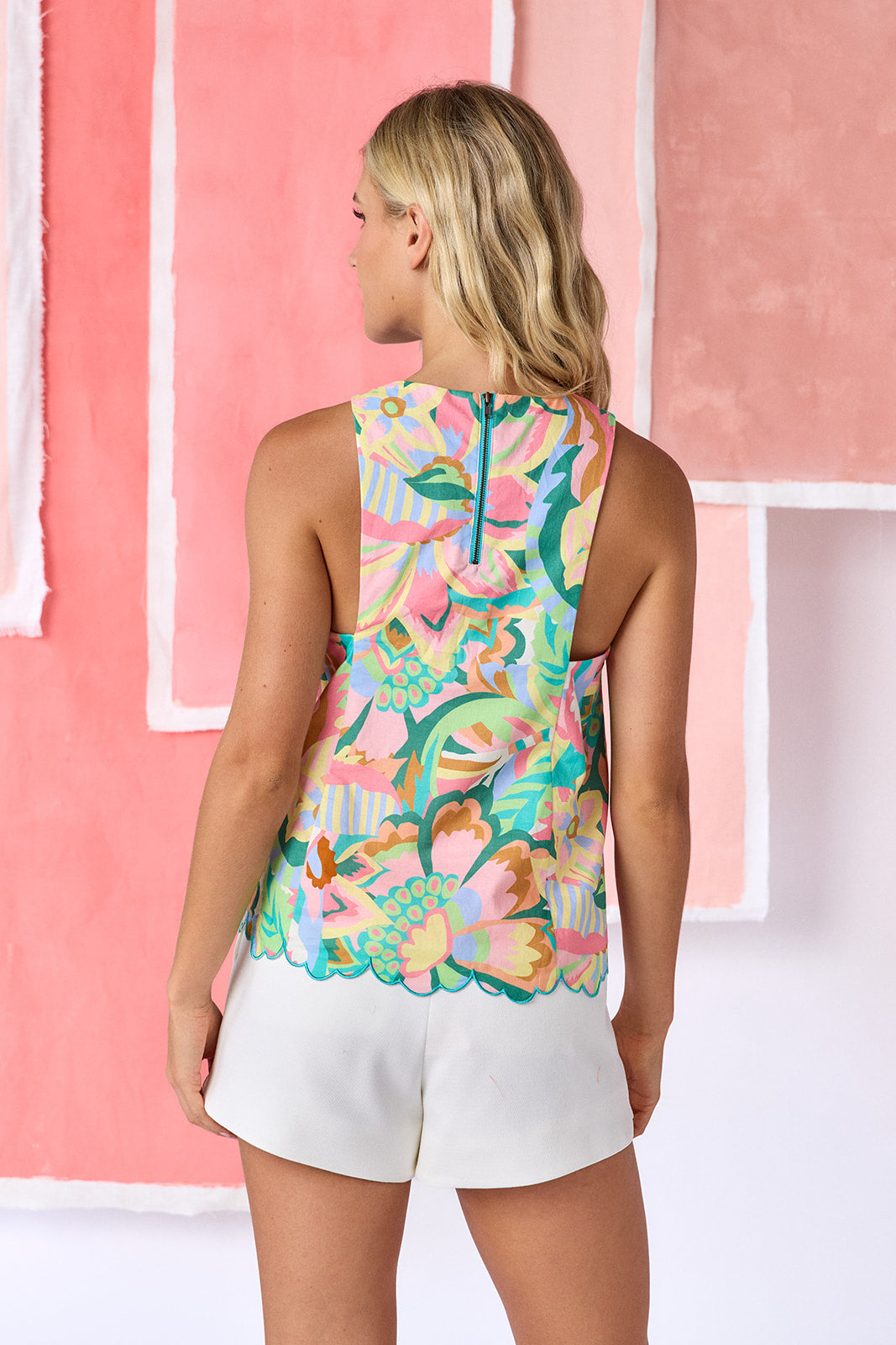 Model wearing relaxed, hip-length sleeveless top in a vibrant multicolor floral print, featuring a high neckline and scalloped hem detail — CROSBY by Mollie Burch