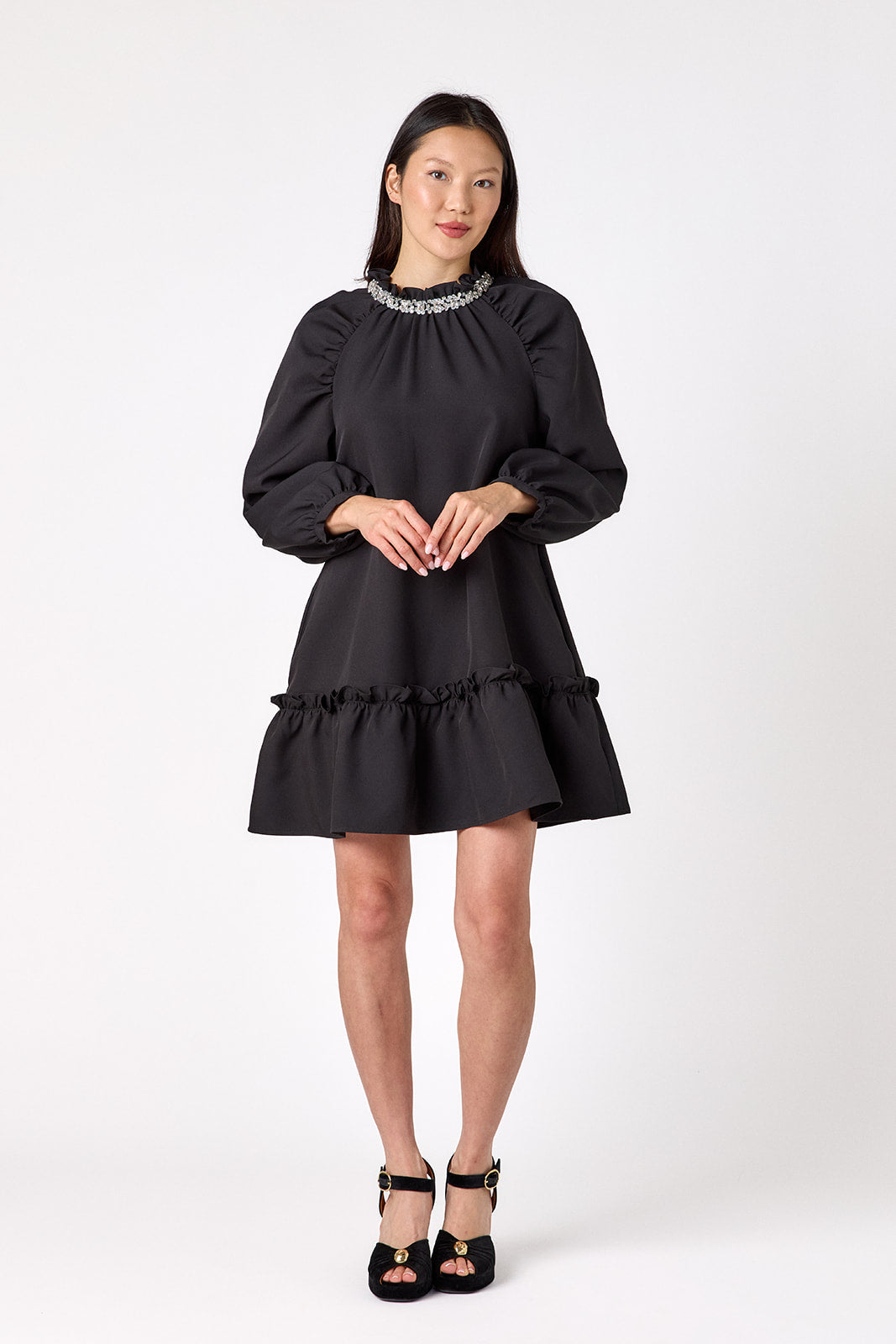 Flynn Dress in Black featuring rhinestone neckline, ruffle hem, and back tie detailing on model – CROSBY by Mollie Burch