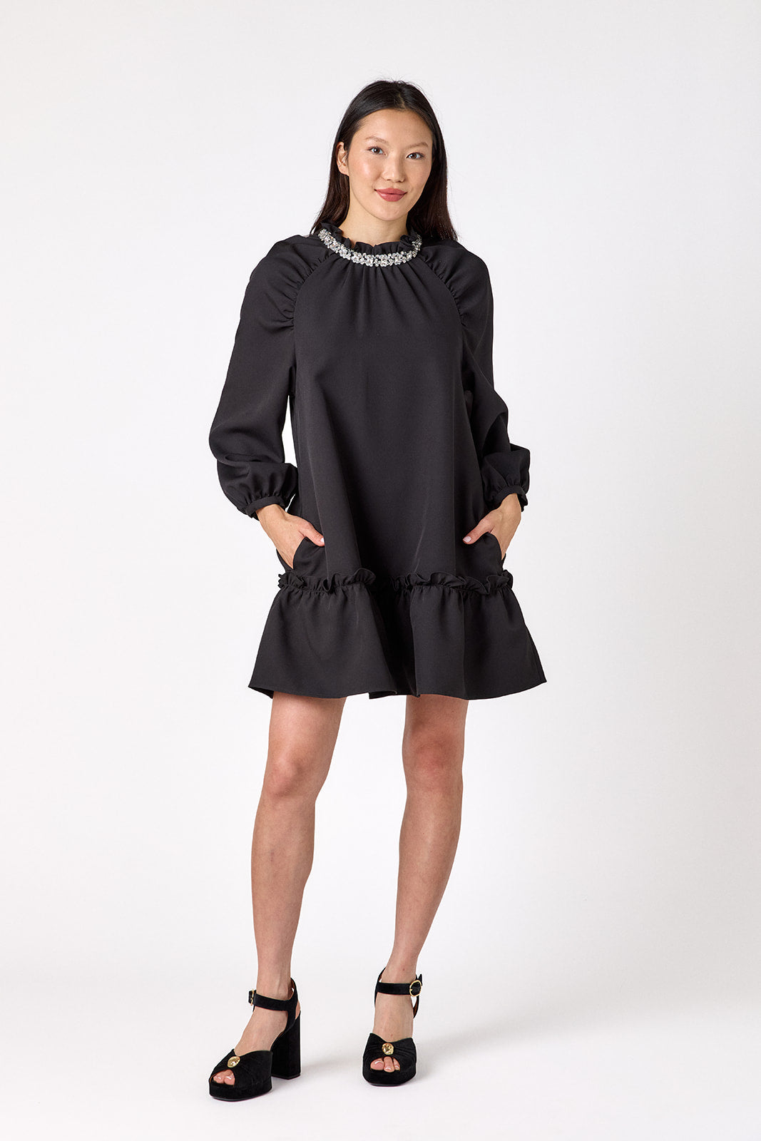 Flynn Dress in Black featuring rhinestone neckline, ruffle hem, and back tie detailing on model – CROSBY by Mollie Burch