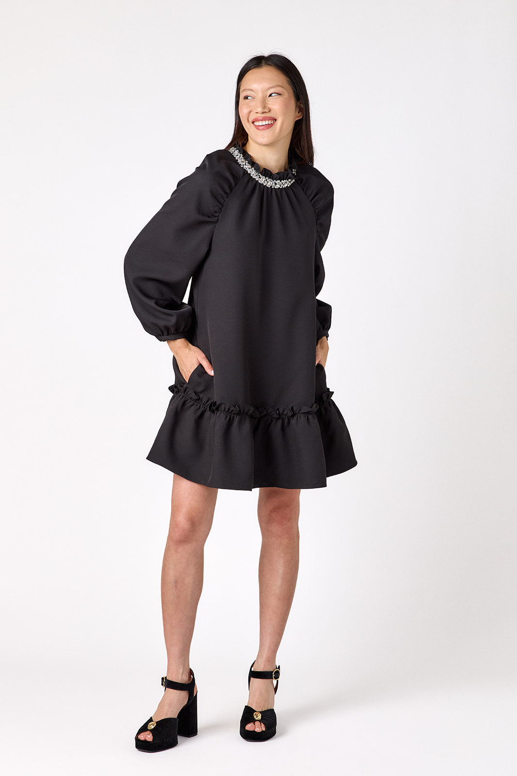 Flynn Dress in Black featuring rhinestone neckline, ruffle hem, and back tie detailing on model – CROSBY by Mollie Burch