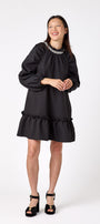 Flynn Dress in Black featuring rhinestone neckline, ruffle hem, and back tie detailing on model – CROSBY by Mollie Burch