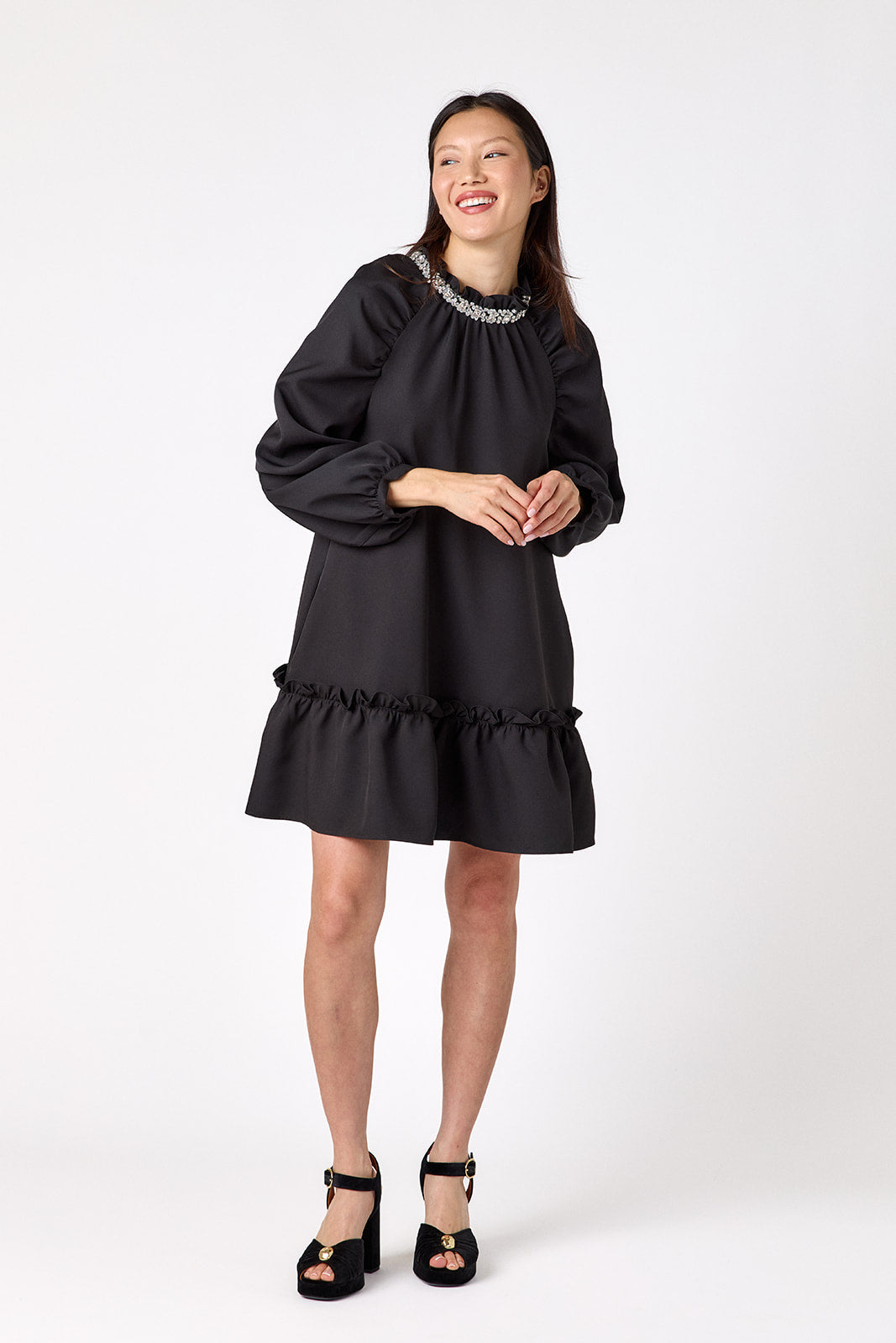 Flynn Dress in Black featuring rhinestone neckline, ruffle hem, and back tie detailing on model – CROSBY by Mollie Burch