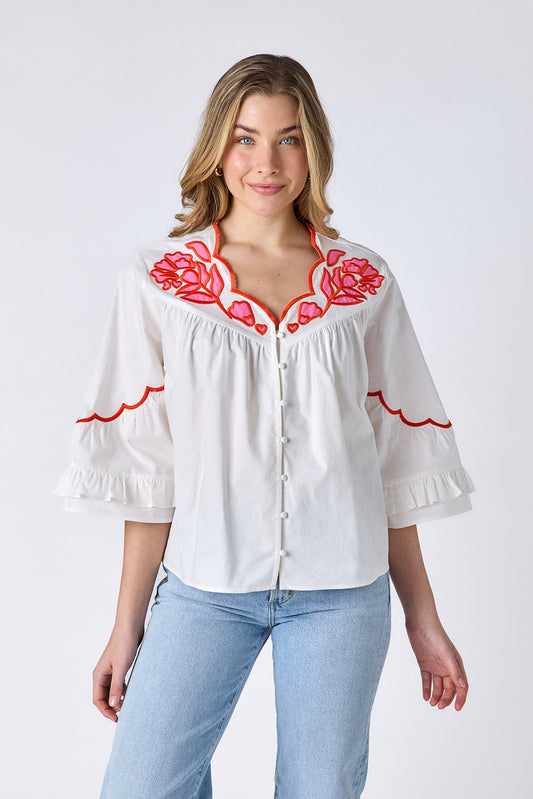 Ivory cotton top with pink and red embroidery, scallop neckline, and button-down front on model — CROSBY by Mollie Burch