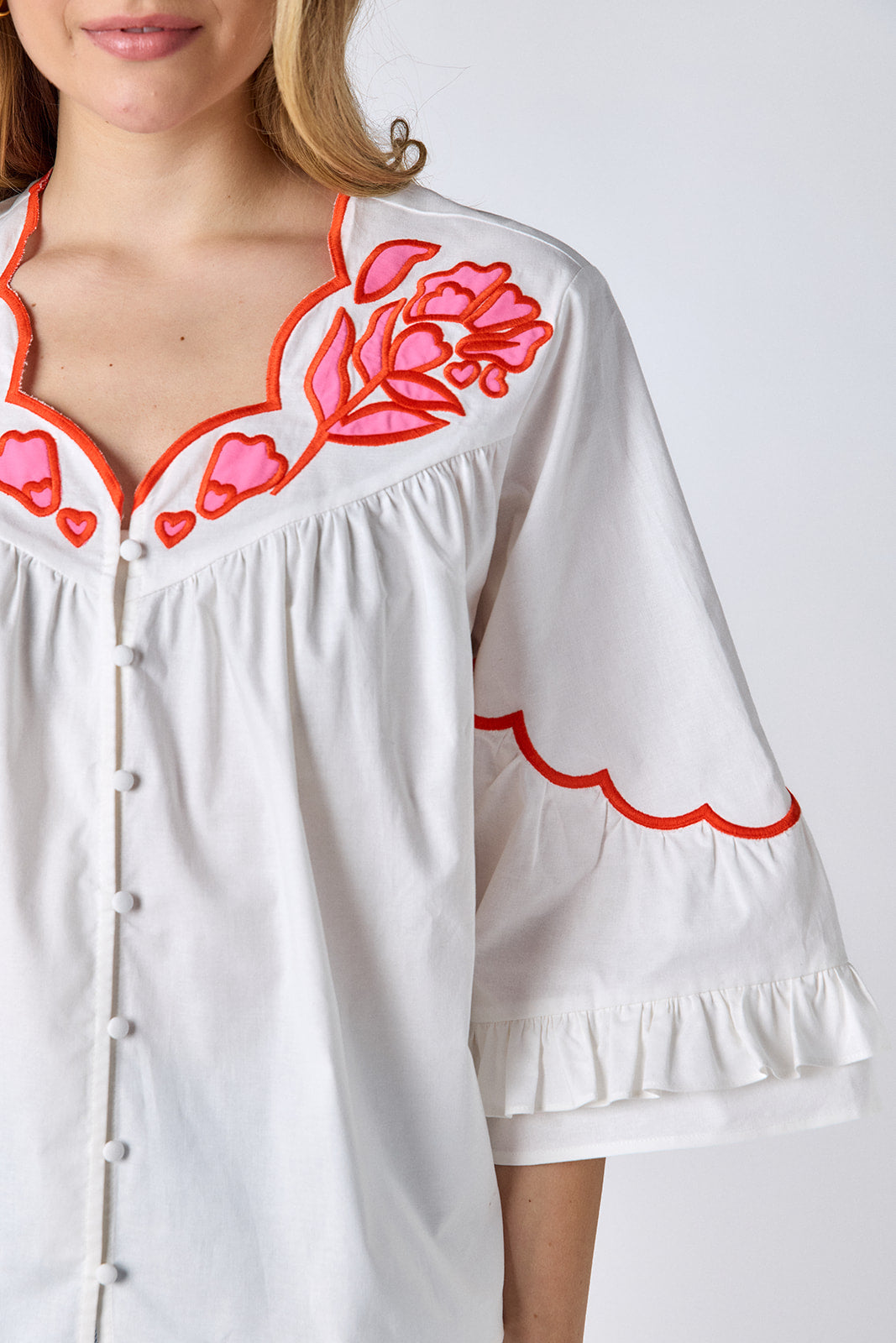 Ivory cotton top with pink and red embroidery, scallop neckline, and button-down front on model — CROSBY by Mollie Burch