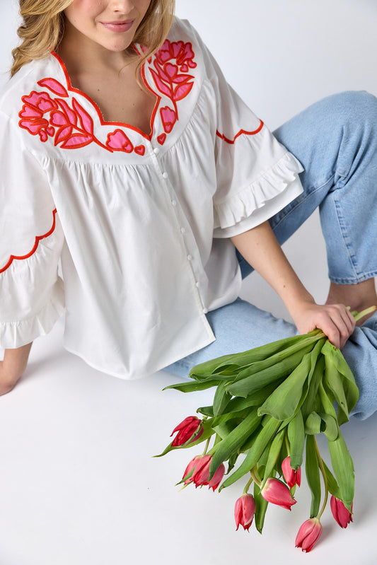Ivory cotton top with pink and red embroidery, scallop neckline, and button-down front on model — CROSBY by Mollie Burch