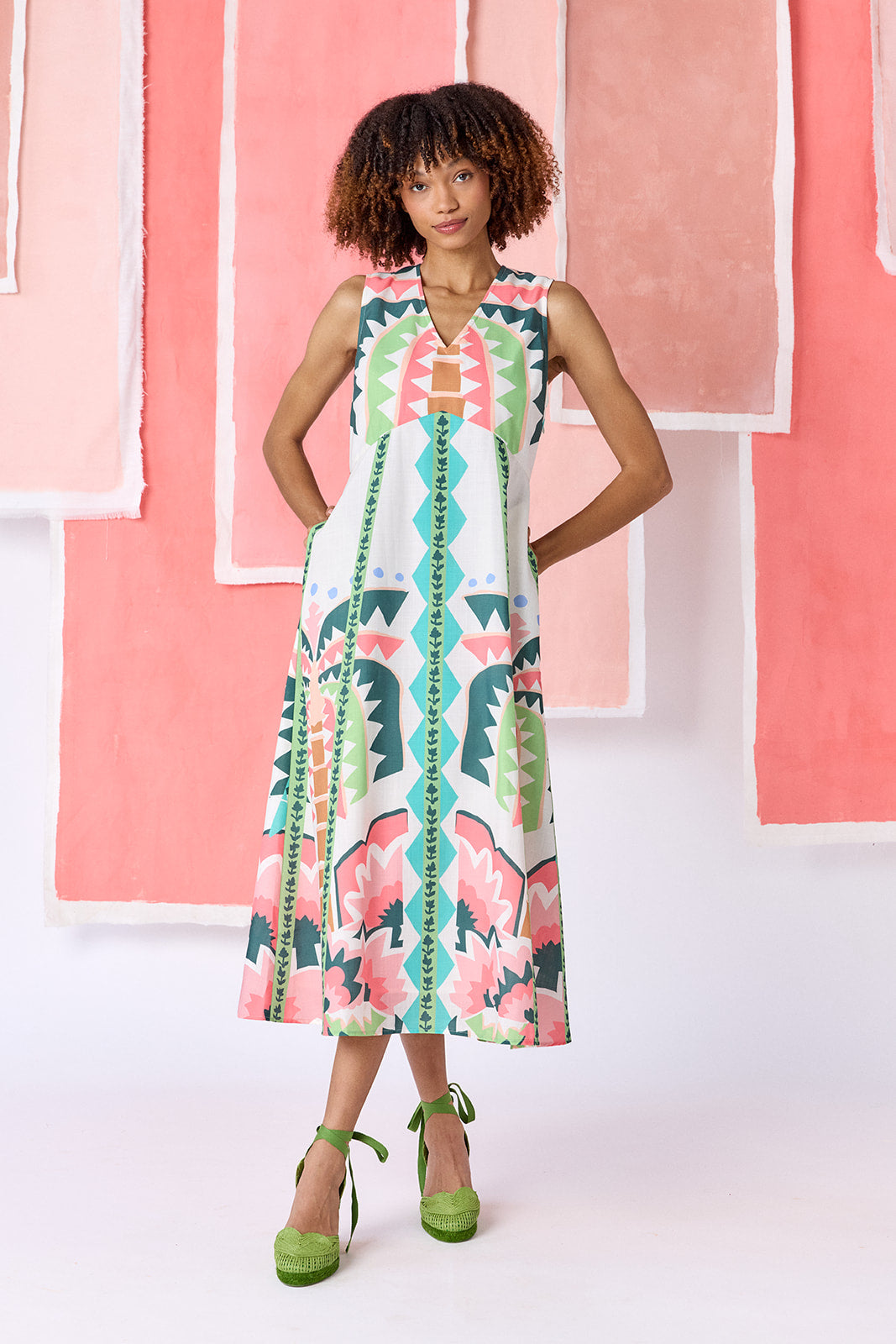 Model wearing ankle-length, sleeveless fit-and-flare dress with a V-neckline and paneled skirt. Features a colorful geometric print in green, coral, light blue, and tan tones — CROSBY by Mollie Burch