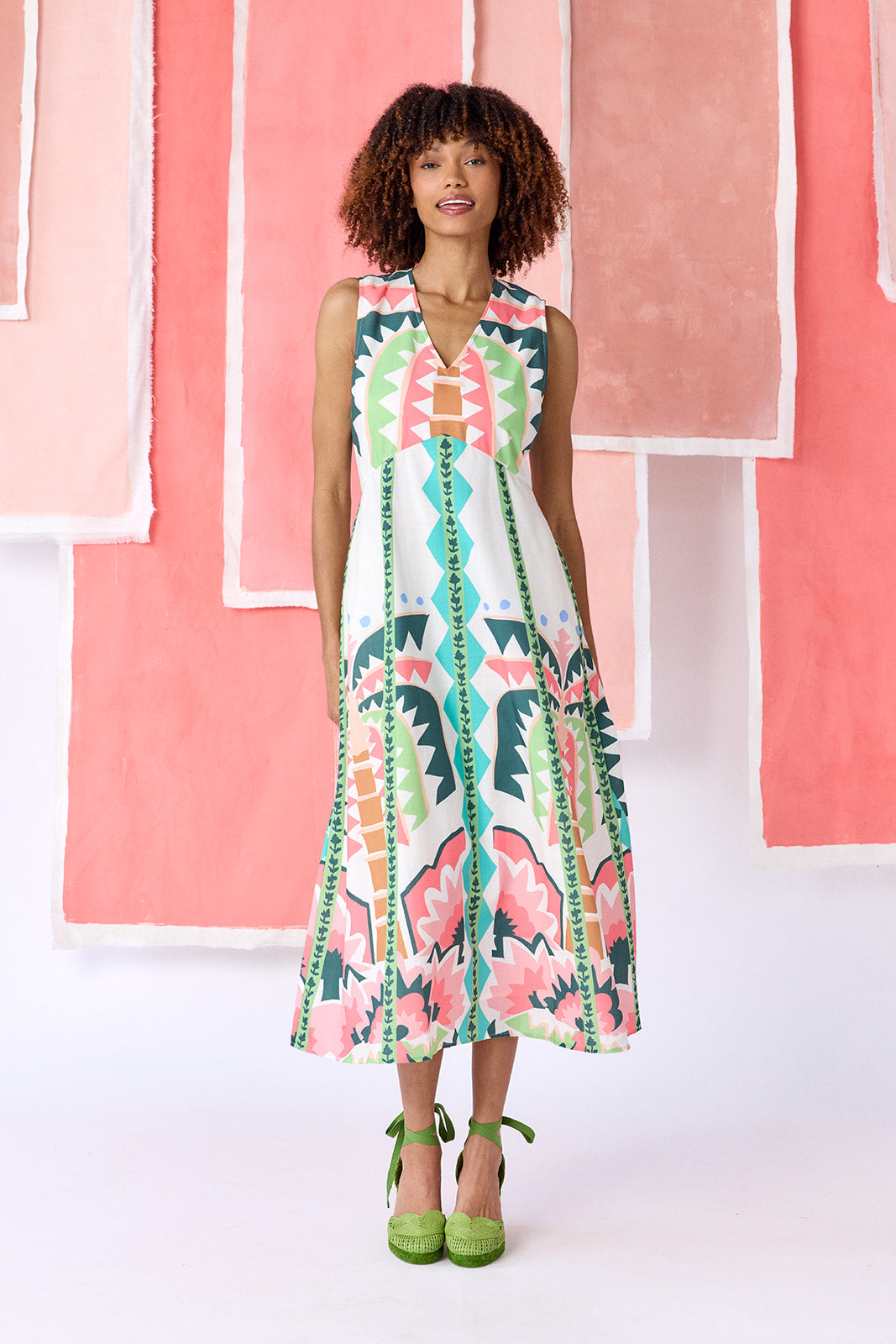 Model wearing ankle-length, sleeveless fit-and-flare dress with a V-neckline and paneled skirt. Features a colorful geometric print in green, coral, light blue, and tan tones — CROSBY by Mollie Burch