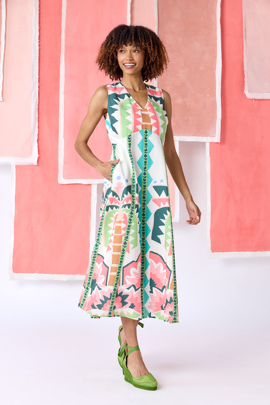 Model wearing ankle-length, sleeveless fit-and-flare dress with a V-neckline and paneled skirt. Features a colorful geometric print in green, coral, light blue, and tan tones — CROSBY by Mollie Burch