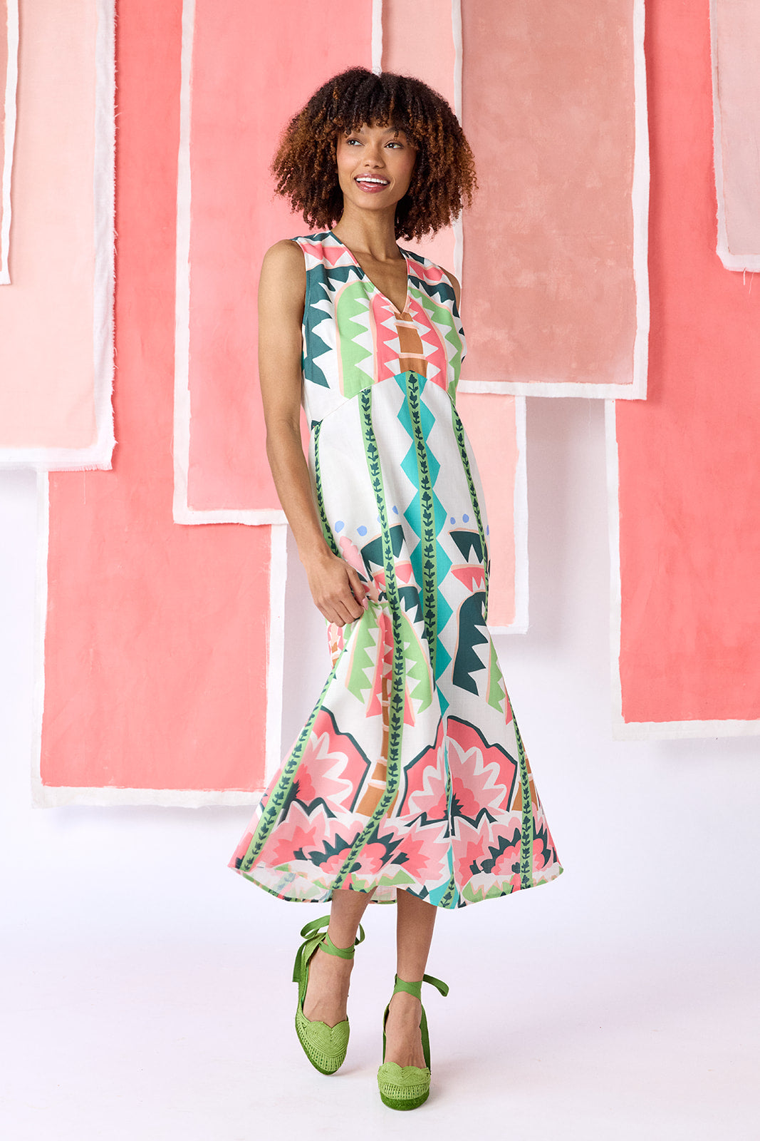 Model wearing ankle-length, sleeveless fit-and-flare dress with a V-neckline and paneled skirt. Features a colorful geometric print in green, coral, light blue, and tan tones — CROSBY by Mollie Burch