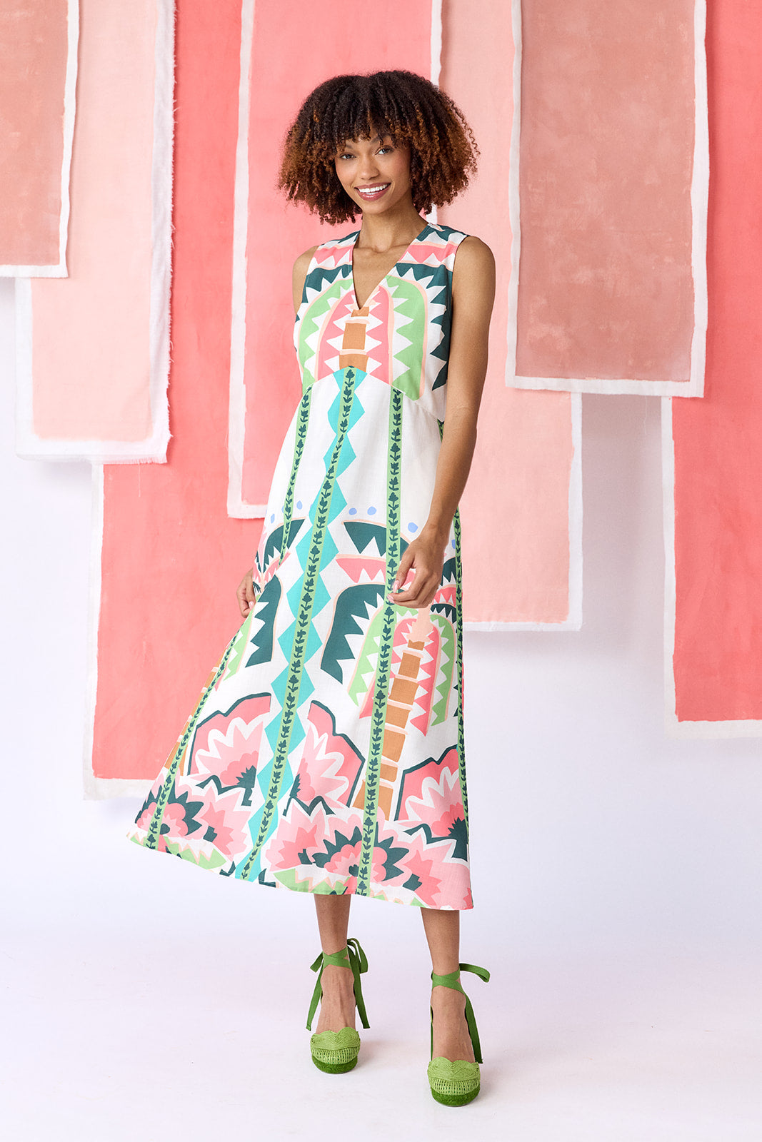 Model wearing ankle-length, sleeveless fit-and-flare dress with a V-neckline and paneled skirt. Features a colorful geometric print in green, coral, light blue, and tan tones — CROSBY by Mollie Burch