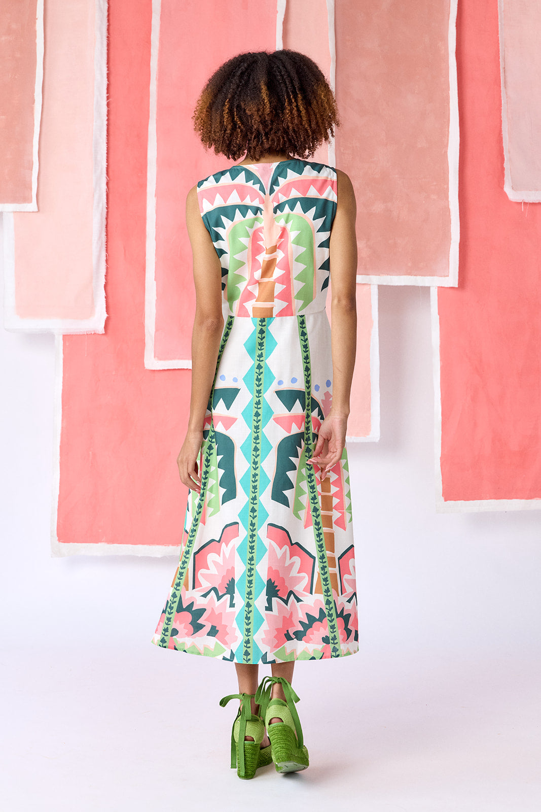 Model wearing ankle-length, sleeveless fit-and-flare dress with a V-neckline and paneled skirt. Features a colorful geometric print in green, coral, light blue, and tan tones — CROSBY by Mollie Burch