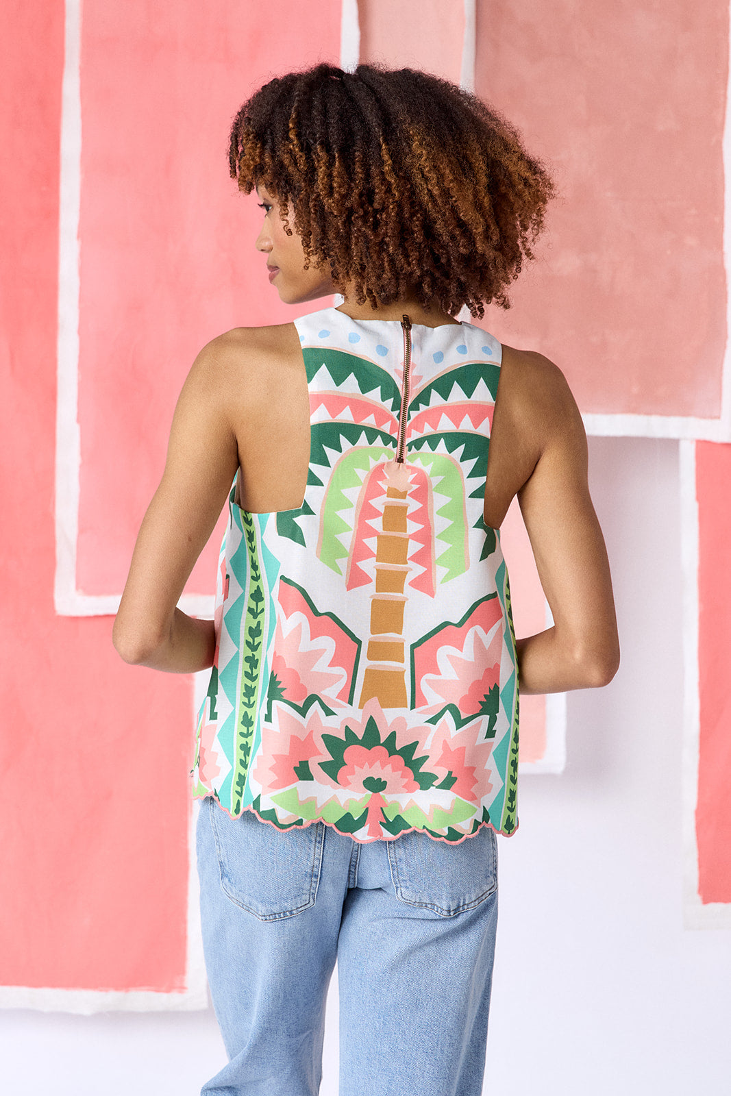 Model wearing hip-length, sleeveless top with a crew neckline and relaxed fit. Features an exposed zipper at the center back, a scalloped embroidered hem, and a colorful geometric print in green, coral, light blue, and tan tones — CROSBY by Mollie Burch