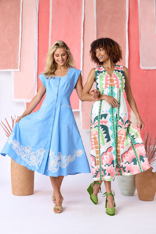 Model wearing a ight blue, mid-calf fit-and-flare dress with a square neckline, cap sleeves, and a full button front. Features a swingy skirt with sheer netting appliqué on the front and scallop-embroidered trim along the neckline and pocket openings — CROSBY by Mollie Burch