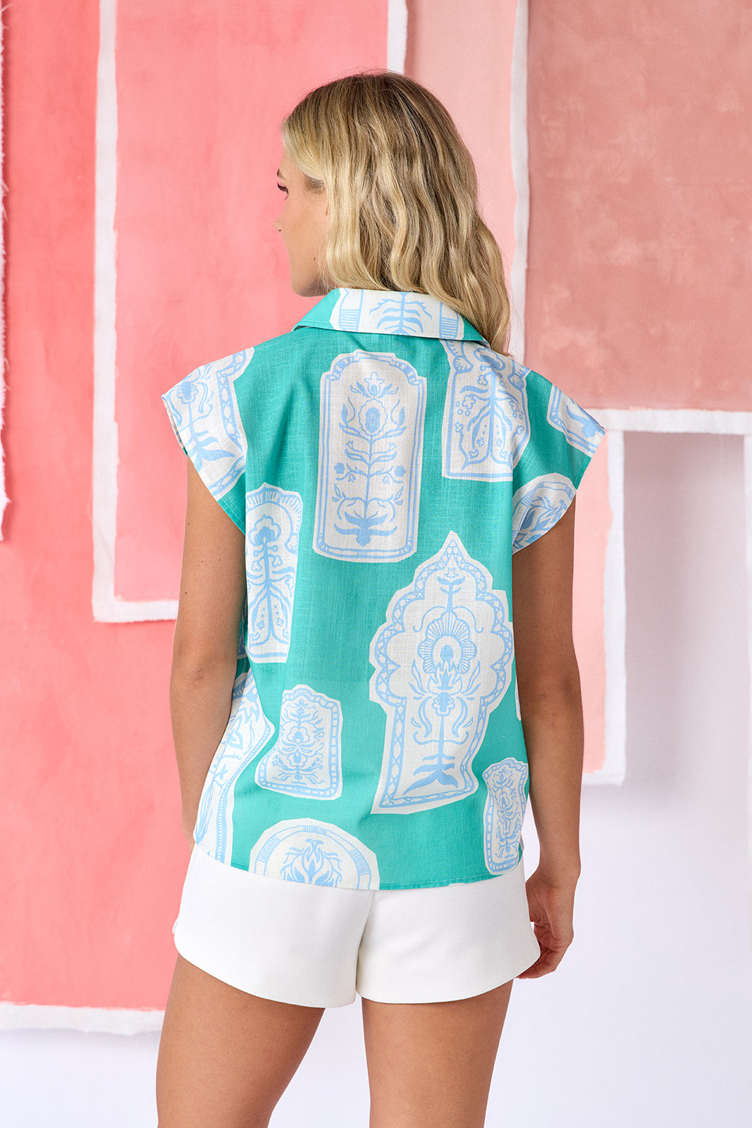 Model wearing sleeveless teal button-down top with a structured collar, featuring a white oversized paisley-style print and slightly flared shoulders  — CROSBY by Mollie Burch