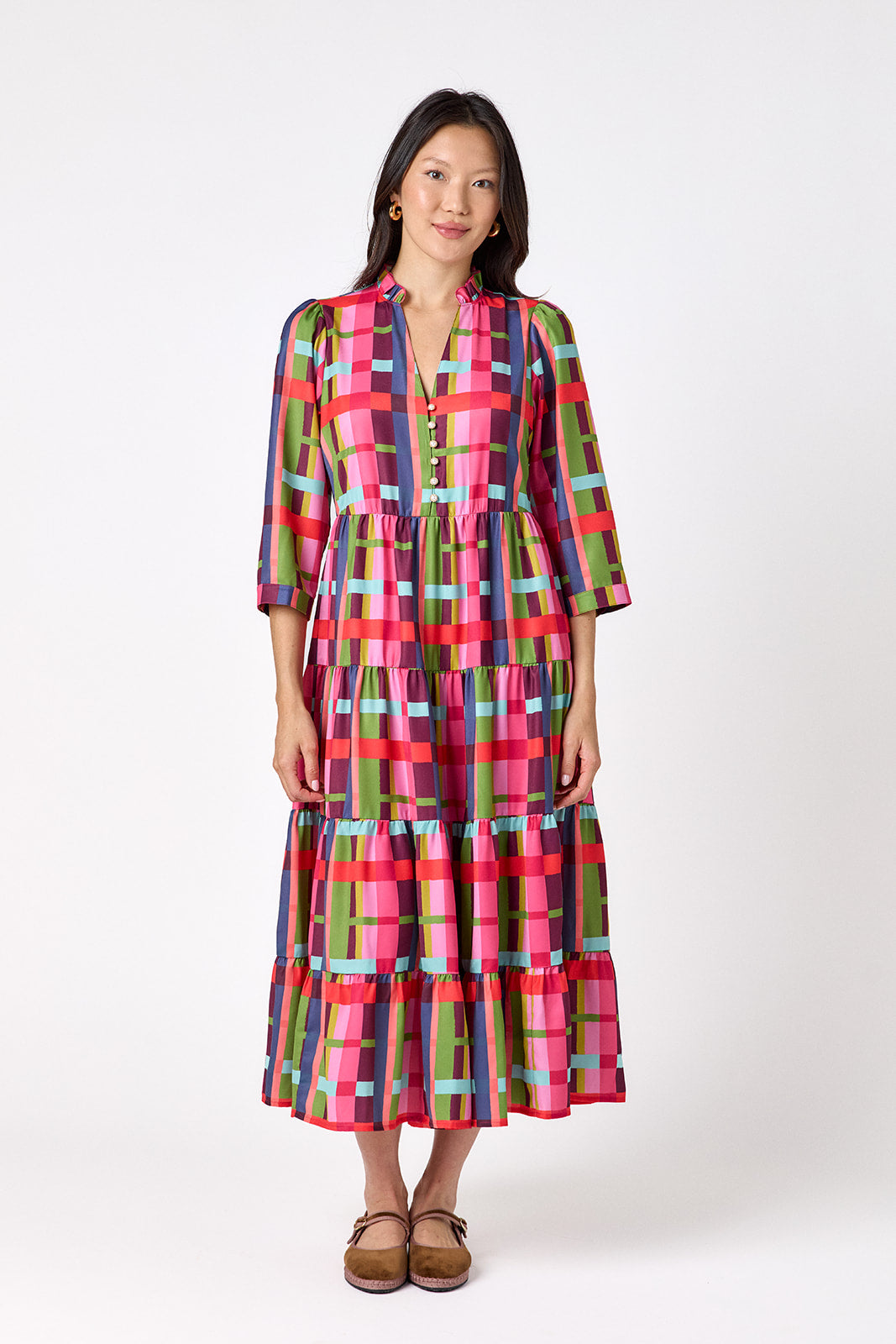 Macrostie Dress in Plaid Parade featuring a colorful plaid print, tiered midi skirt, and gold-accented buttons on model – CROSBY by Mollie Burch
