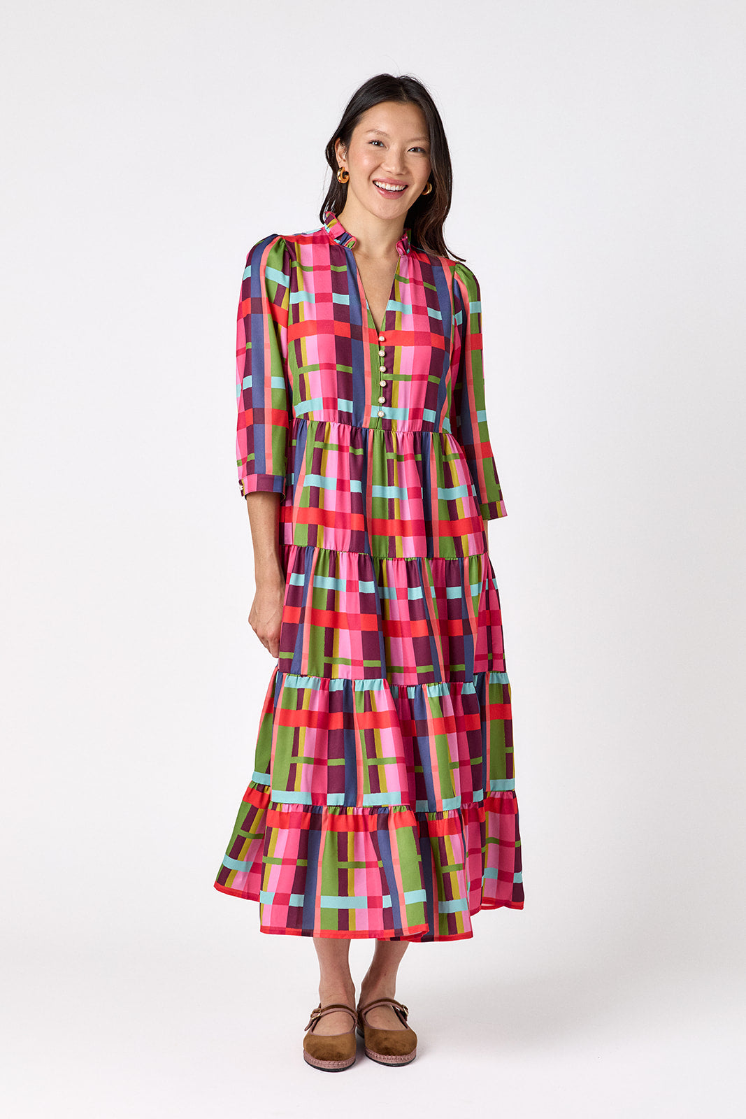 Macrostie Dress in Plaid Parade featuring a colorful plaid print, tiered midi skirt, and gold-accented buttons on model – CROSBY by Mollie Burch