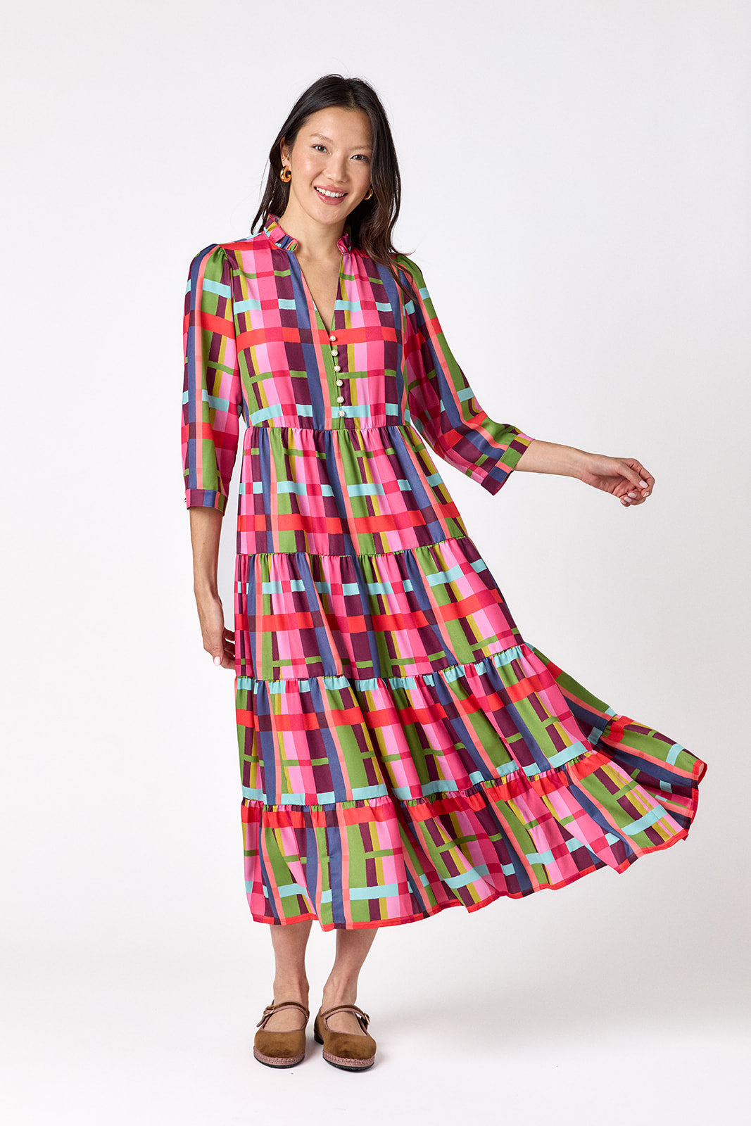 Macrostie Dress in Plaid Parade featuring a colorful plaid print, tiered midi skirt, and gold-accented buttons on model – CROSBY by Mollie Burch