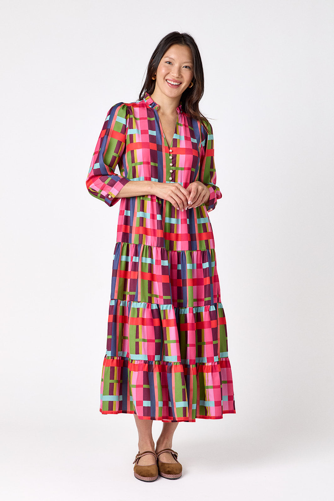 Macrostie Dress in Plaid Parade featuring a colorful plaid print, tiered midi skirt, and gold-accented buttons on model – CROSBY by Mollie Burch