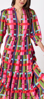 Macrostie Dress in Plaid Parade featuring a colorful plaid print, tiered midi skirt, and gold-accented buttons on model – CROSBY by Mollie Burch