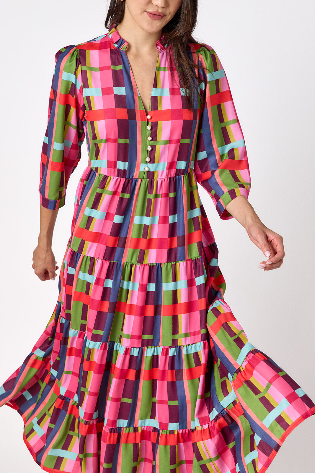 Macrostie Dress in Plaid Parade featuring a colorful plaid print, tiered midi skirt, and gold-accented buttons on model – CROSBY by Mollie Burch
