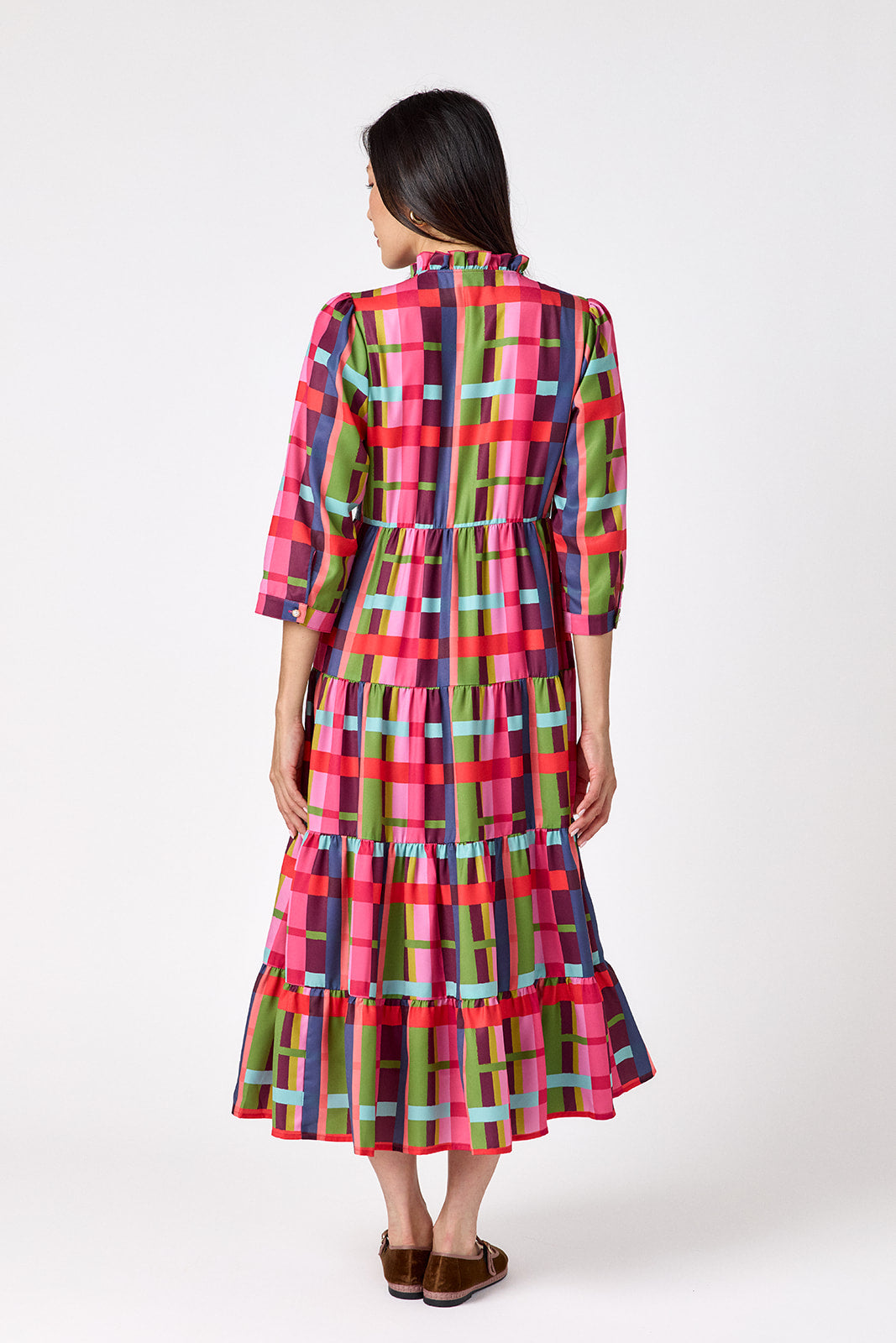 Macrostie Dress in Plaid Parade featuring a colorful plaid print, tiered midi skirt, and gold-accented buttons on model – CROSBY by Mollie Burch