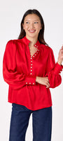 Leland Blouse in Ruby Red featuring puff sleeves and gold-rimmed pearl buttons on model – CROSBY by Mollie Burch