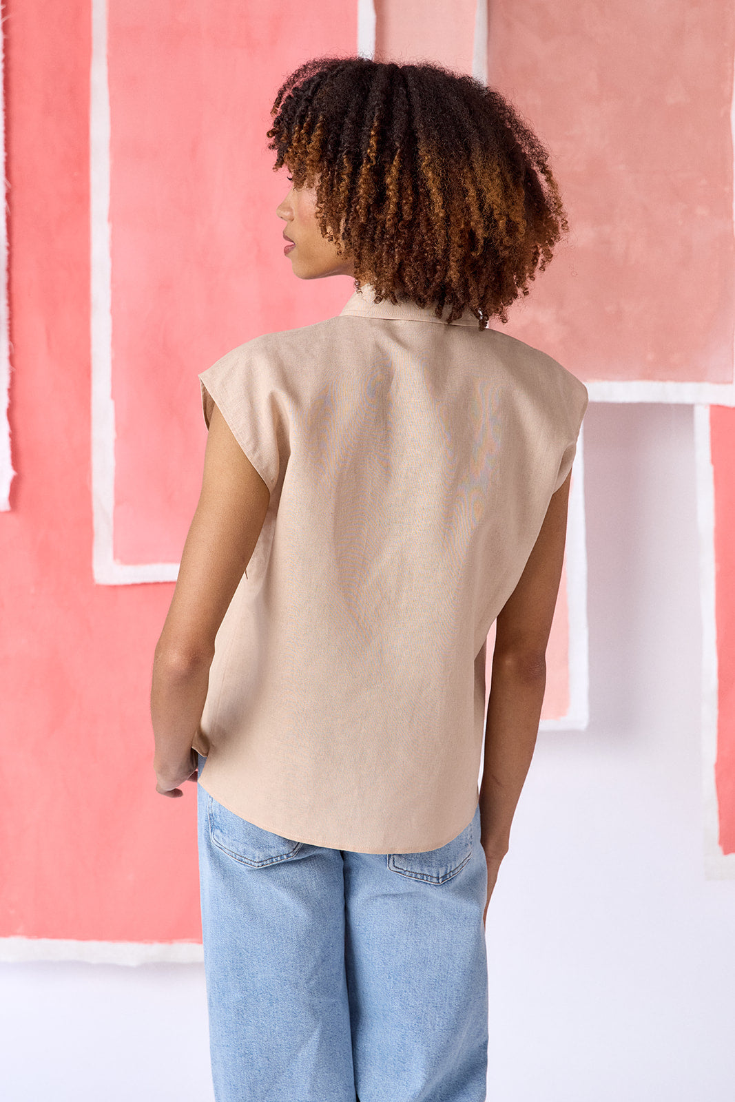 Model wearing beige, hip-length relaxed top with cap sleeves and a squiggle button placket, finished with contrast trim — CROSBY by Mollie Burch