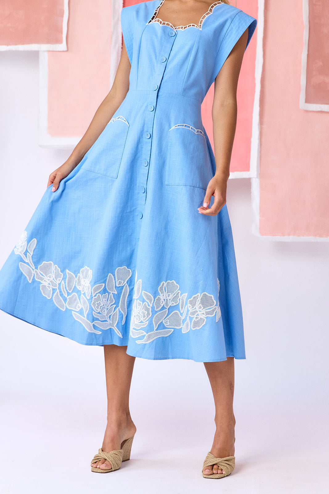 Model wearing a ight blue, mid-calf fit-and-flare dress with a square neckline, cap sleeves, and a full button front. Features a swingy skirt with sheer netting appliqué on the front and scallop-embroidered trim along the neckline and pocket openings — CROSBY by Mollie Burch