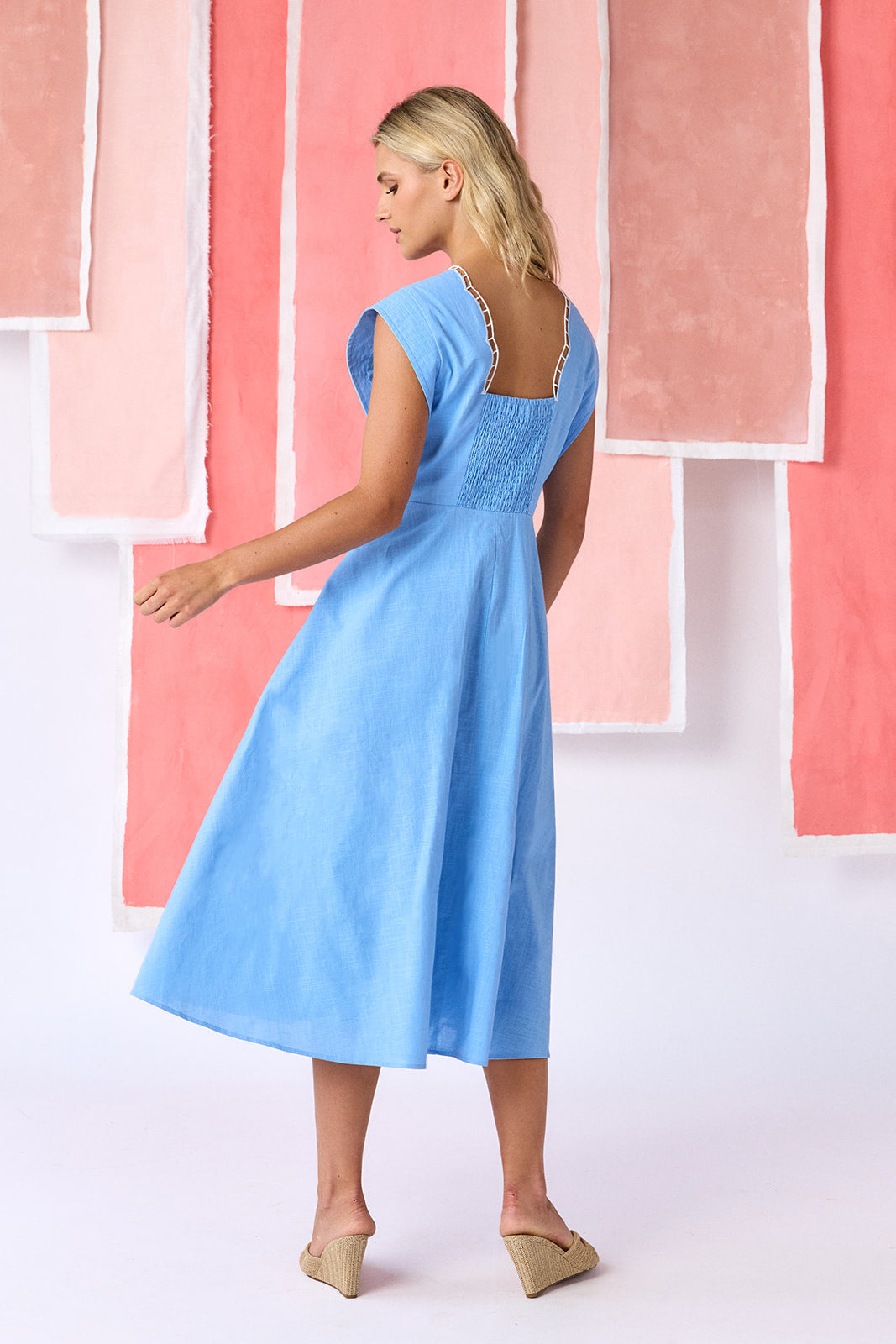 Model wearing a ight blue, mid-calf fit-and-flare dress with a square neckline, cap sleeves, and a full button front. Features a swingy skirt with sheer netting appliqué on the front and scallop-embroidered trim along the neckline and pocket openings — CROSBY by Mollie Burch