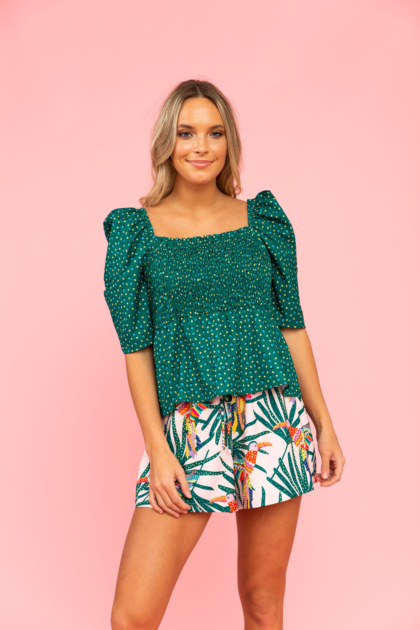 Green top with smocked bodice and peplum silhouette and shorts with parrot and leaf pattern