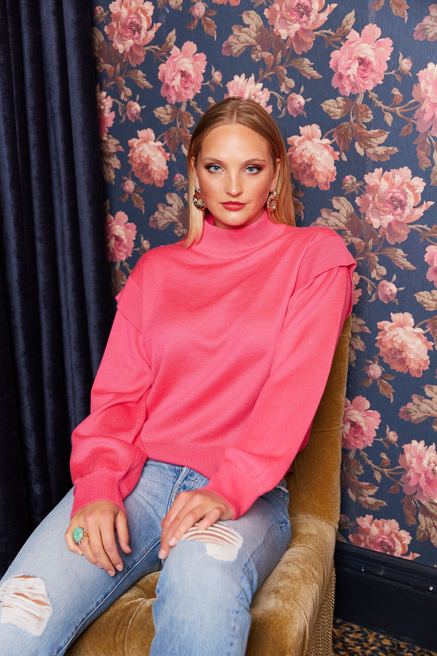 Woman in bright pink mock neck sweater against floral backdrop