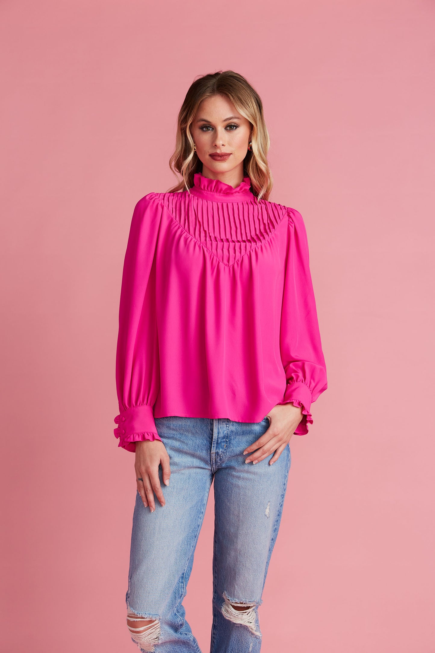 Woman in bright pink blouse with high collar and pleating details on the chest