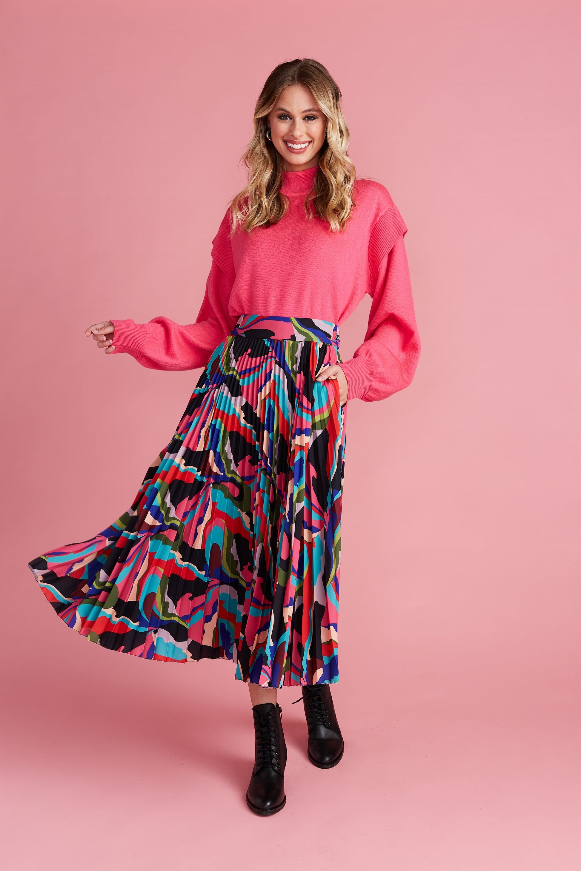 Woman in pink mock neck sweater paired with colorful pleated midi skirt