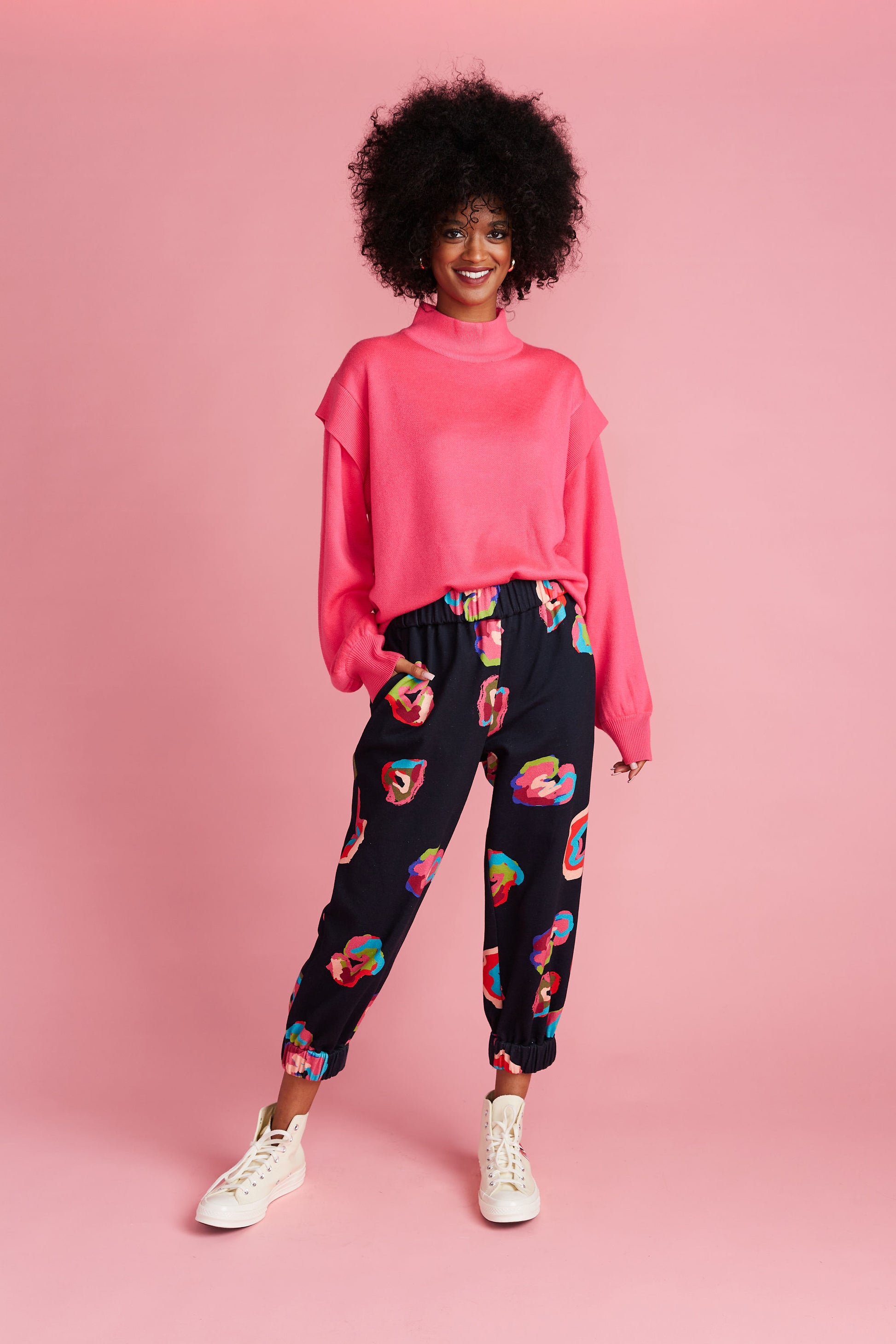Woman in pink mock neck sweater paired with black joggers with colorful leopard spots