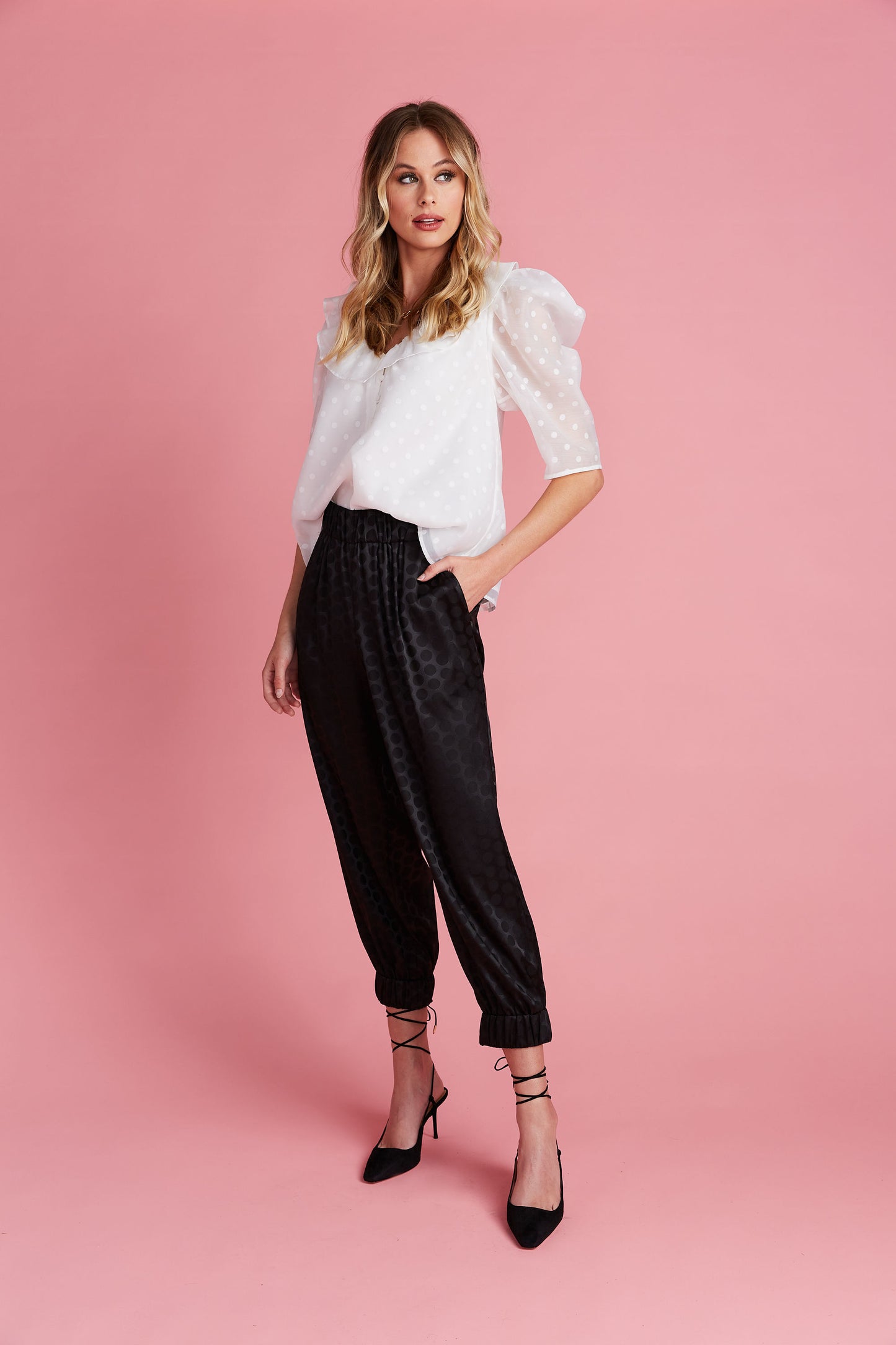 Woman in v-neck white puff sleeve blouse with polka dot pattern and black silky polka dot joggers